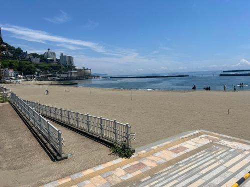 a sandy beach with a fence and the ocean at ゲストハウスあさひ in Atami