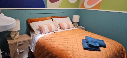 a bedroom with a bed with an orange blanket and two lamps at Arty Apartments in Tauranga