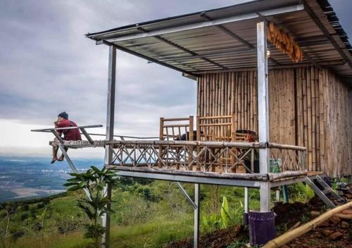 a man sitting on a balcony of a building on a hill at ดอยสะโง้วิวโฮมสเตย์บ้านริมผา in Chiang Saen