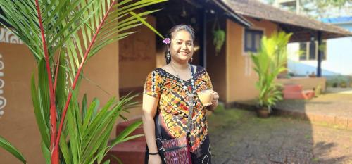a woman is standing next to a plant at Kudil Mud Cottages, Cheemeni in Peringom
