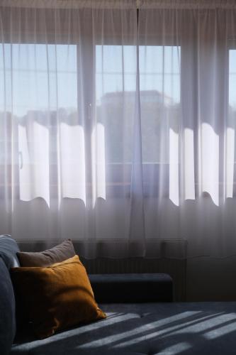 a couch with a pillow in front of a window at Trón Apartman 2 in Siklós