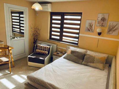 a bedroom with a bed and a chair and windows at Къща за гости Василеви in Bratsigovo