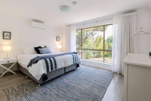 a white bedroom with a bed and a large window at Capewood - Coastal Family Retreat in Prevelly in Prevelly