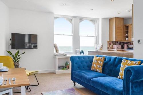 a living room with a blue couch and a kitchen at Stylish Flat with Stunning Sea Views Ilfracombe in Ilfracombe