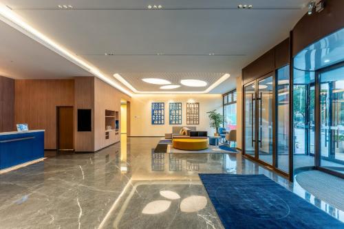 an office lobby with a yellow couch and tables and windows at Holiday Inn Express Luoyang Longmen by IHG in Luoyang