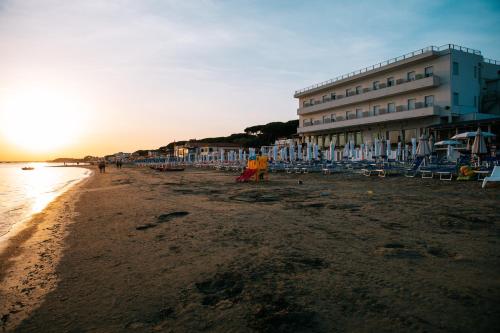 a beach with a building and chairs and the ocean at Hotel Parrini in Follonica