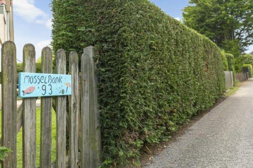 a wooden fence with a sign on it next to a hedge at Mosselbank 93 - Noordzeepark Ouddorp, with private front and back garden near the beach - not for companies in Ouddorp