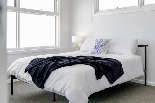 a bed with a black and white comforter and two windows at Coastal Dreams (#1) in Dromana