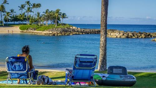 a woman sitting in lawn chairs next to the ocean at Coconut Plantation 1086-4 in Kapolei