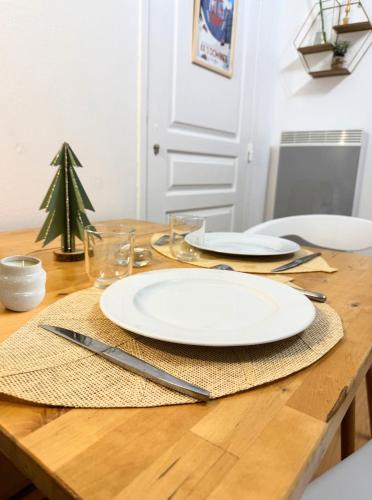 a wooden table with two white plates and a christmas tree at AX proche départ rando - piscine - parking gratuit in Ax-les-Thermes