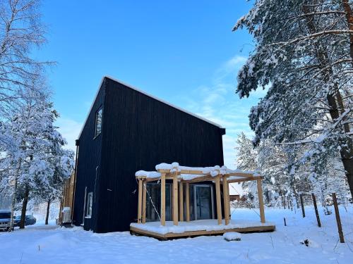 a cabin in the snow next to a black building at GRANIASTY - nowoczesny dom wakacyjny z basenem in Smażyno