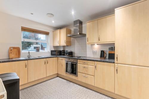 a large kitchen with wooden cabinets and a window at Redhill,Sleeps9,Parking,17minsLGW30 to London in Merstham