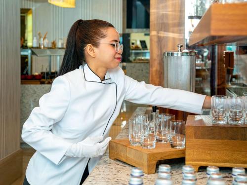 a woman in a kitchen preparing wine glasses at Mövenpick Hotel & Apartments Ghala Muscat in Muscat