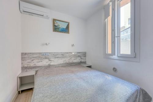 un lit dans une chambre blanche avec une fenêtre dans l'établissement Le Patio du Port - Appt climatisé avec jardin, à Sanary-sur-Mer