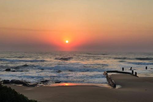 a sunset over the ocean with a pier in the sand at Emanzini Self-catering guesthouse in Mtwalume