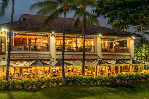 a building with a restaurant with tables and umbrellas at Coconut Plantation 1110-3 in Kapolei