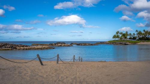 a beach with rocks in the water and a fence at Coconut Plantation 1078-3 in Kapolei