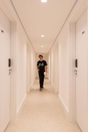 a man walking down a corridor in a white hallway at ZEST Pedroso in Sao Paulo