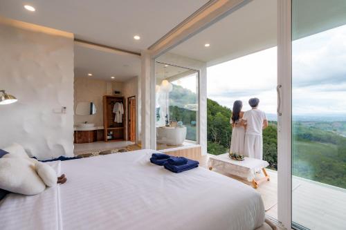 a man and woman standing in a bedroom with a large window at Make me see cloud - Chiang rai in Mae Suai