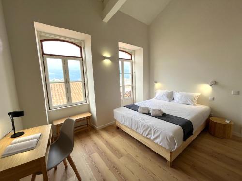 a bedroom with a bed and a desk and two windows at Casas de Alpedide in Coimbra