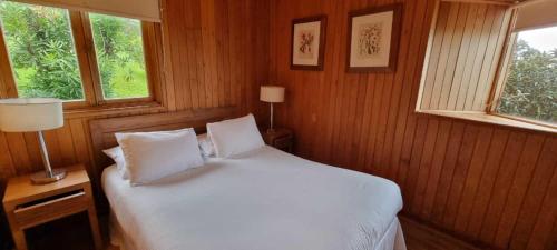 a bedroom with a white bed with two windows at Hotel y Cabañas Lago Ranco - Caja los Andes in Futrono