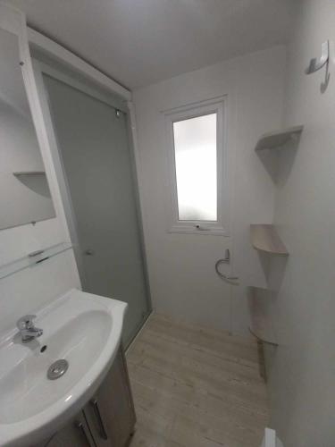une salle de bain blanche avec un lavabo et une fenêtre dans l'établissement MH 515 AMIRA TOUT CONFORT 3ch et 2sdb dans camping 4étoiles avec parc aquatique, à Saint-Julien-en-Born