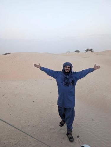 a man standing in the desert with his arms outstretched at Camp Privé rêve de désert in Douz
