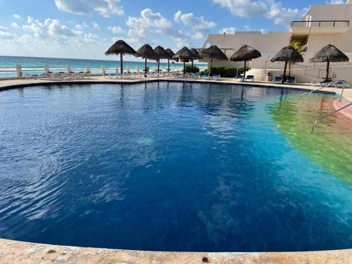 a large swimming pool next to a beach with umbrellas at Condominio Privado Villas Marlin Zona Hotelera Cancun in Cancún