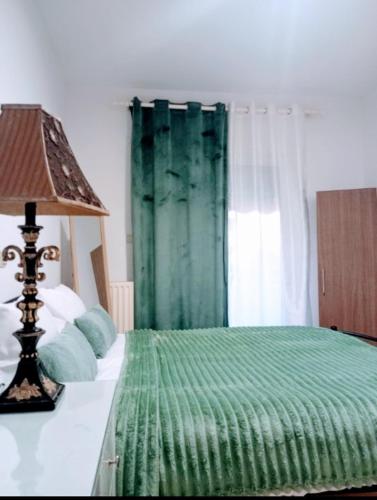 a bedroom with a bed with a green blanket and a lamp at Siame in Drama