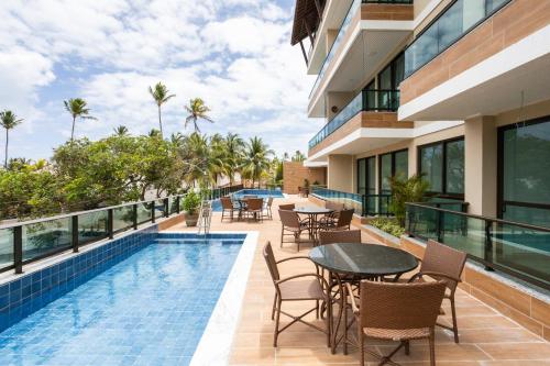eine Außenterrasse mit Tischen und Stühlen neben einem Pool in der Unterkunft Capri Residence in Porto De Galinhas