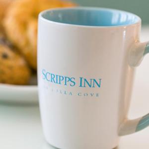 a white coffee cup sitting on a table with a plate of food at Scripps Inn in San Diego