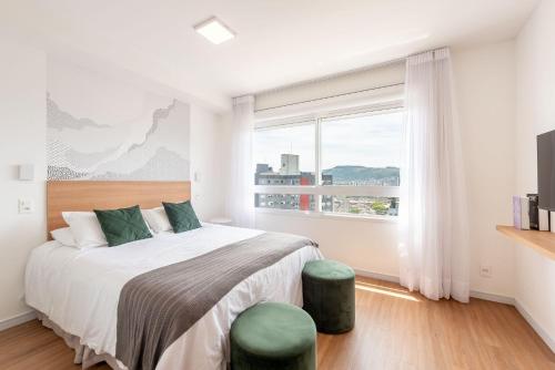 a white bedroom with a bed and a large window at Connect by LikeHome in Porto Alegre