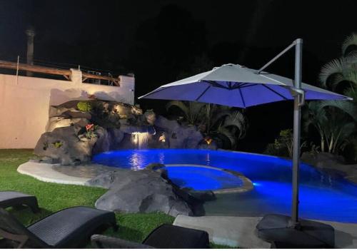 a blue pool with an umbrella and some chairs at Casa VIP con la mejor vista de Lomas de Cocoyoc in Texcalpan