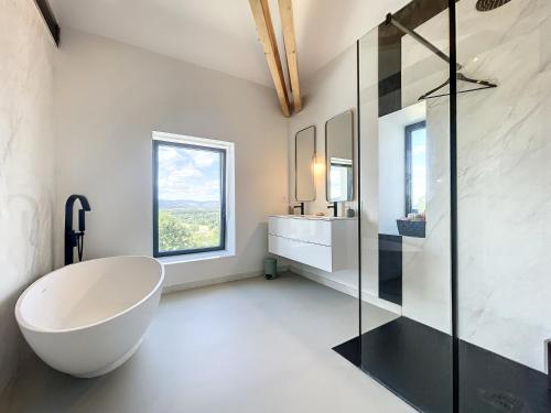 La salle de bains est pourvue d'une grande baignoire blanche et d'une fenêtre. dans l'établissement Domaine de l'Heure Bleue, à Genouilleux