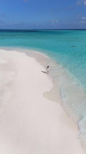 a person walking on a white beach in the ocean at Ahiva Village in Fulhadhoo
