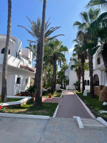 a walkway in front of a white house with palm trees at Appartement pied sur mer in Fnidek