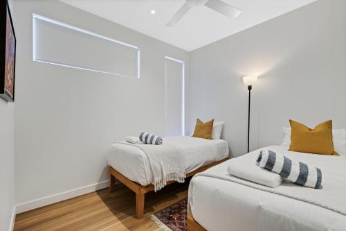two beds in a room with white walls and yellow pillows at Breathtaking Beachfront 3 Bedroom Penthouse Bokarina Sunshine Coast in Bokarina