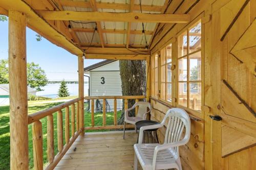 a wooden porch with two white chairs on it at Chippewa Bluffs Resort Spacious Combined 2BR 2BA Cabins in Barryton