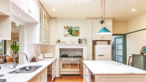 eine Küche mit weißen Schränken, einer Spüle und einem Kühlschrank in der Unterkunft Kookaburra Cottage Pearl Beach in Pearl Beach