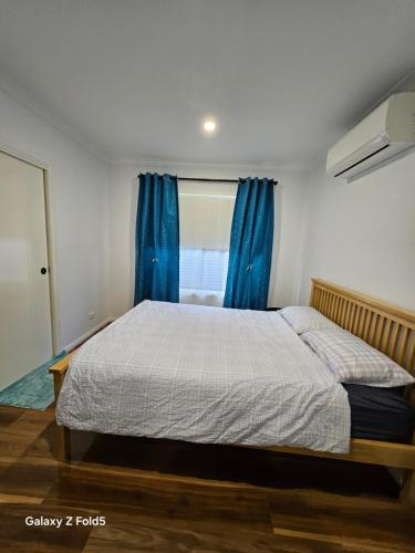 una camera da letto con un letto con tende blu e una finestra di Melton Cozy Home a Melton South