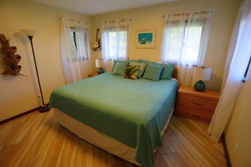 a bedroom with a bed with green sheets and windows at kehena black sand beach house - ocean view swim spa in Pahoa
