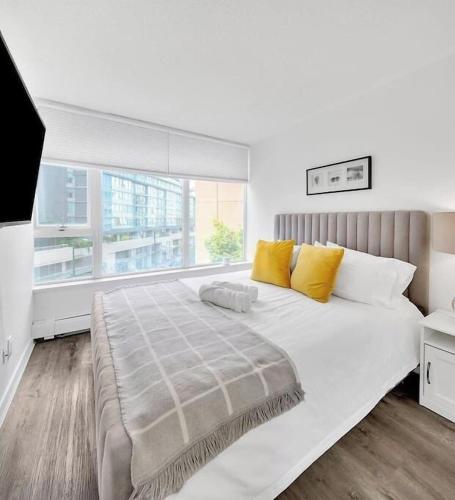 a white bedroom with a large bed with yellow pillows at Stylish Condo in Downtown in Vancouver