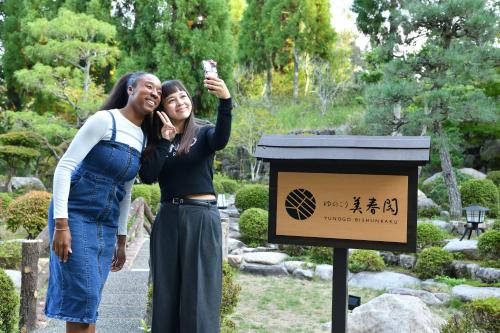 two women standing next to a sign in a garden at Yunogo Onsen HOTEL YUNOMORI BISYUNKAKU in Mimasaka