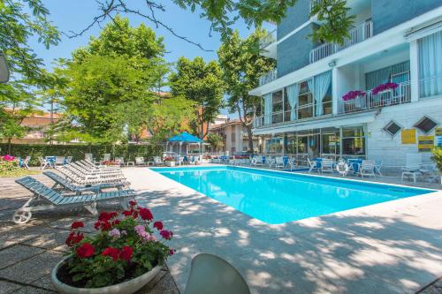 a swimming pool with chairs and flowers next to a building at Hotel Gioiello in Cesenatico