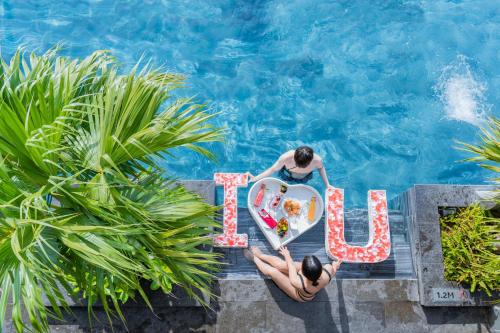 岘港Peninsula Hotel Danang的泳池里有两个人，旁边立着一块牌子，上面写着“爱”。