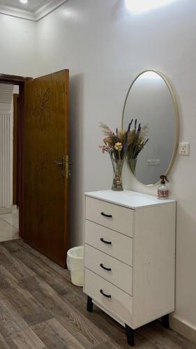 a dresser with a mirror and a vase with flowers on it at شقة رائعة لسياحة في جازان in Jazan