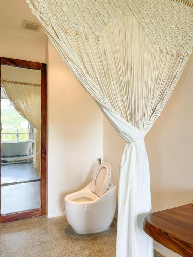 a bathroom with a toilet and a curtain at La Grotta Hotel - Phu Quoc Emerald Bay in Phu Quoc