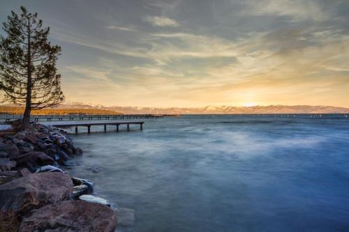 a lake with a pier and a tree on the shore at Henderson by AvantStay Lake View Walk to Beach Garwoods More in Carnelian Bay