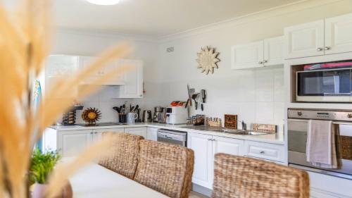 Una cocina con gabinetes blancos y una mesa y sillas. en Sunshine Shack - Umina Beach, en Umina Beach 