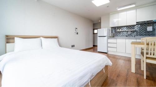 a white bedroom with a white bed and a kitchen at jeju ondamhouse pension in Jeju